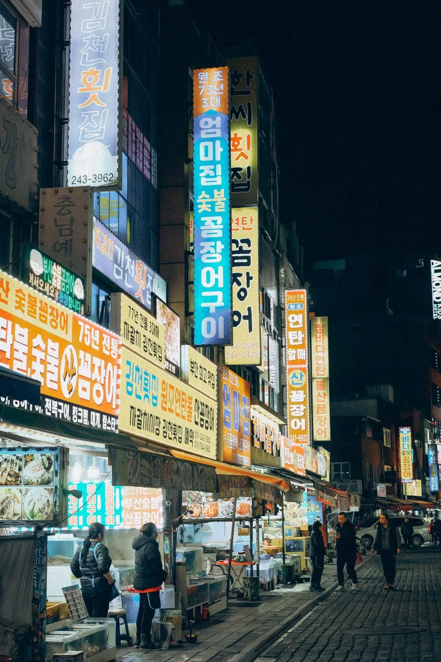 Explore the bustling night market streets of Seoul, South Korea, illuminated by colorful neon signs.