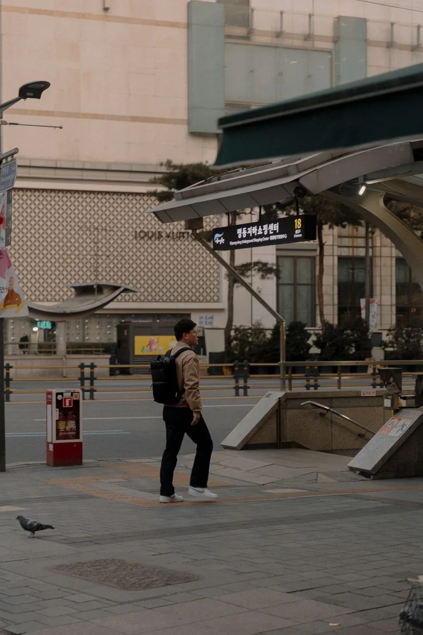 Pedestrian near a subway entrance in a bustling South Korea urban street scene.