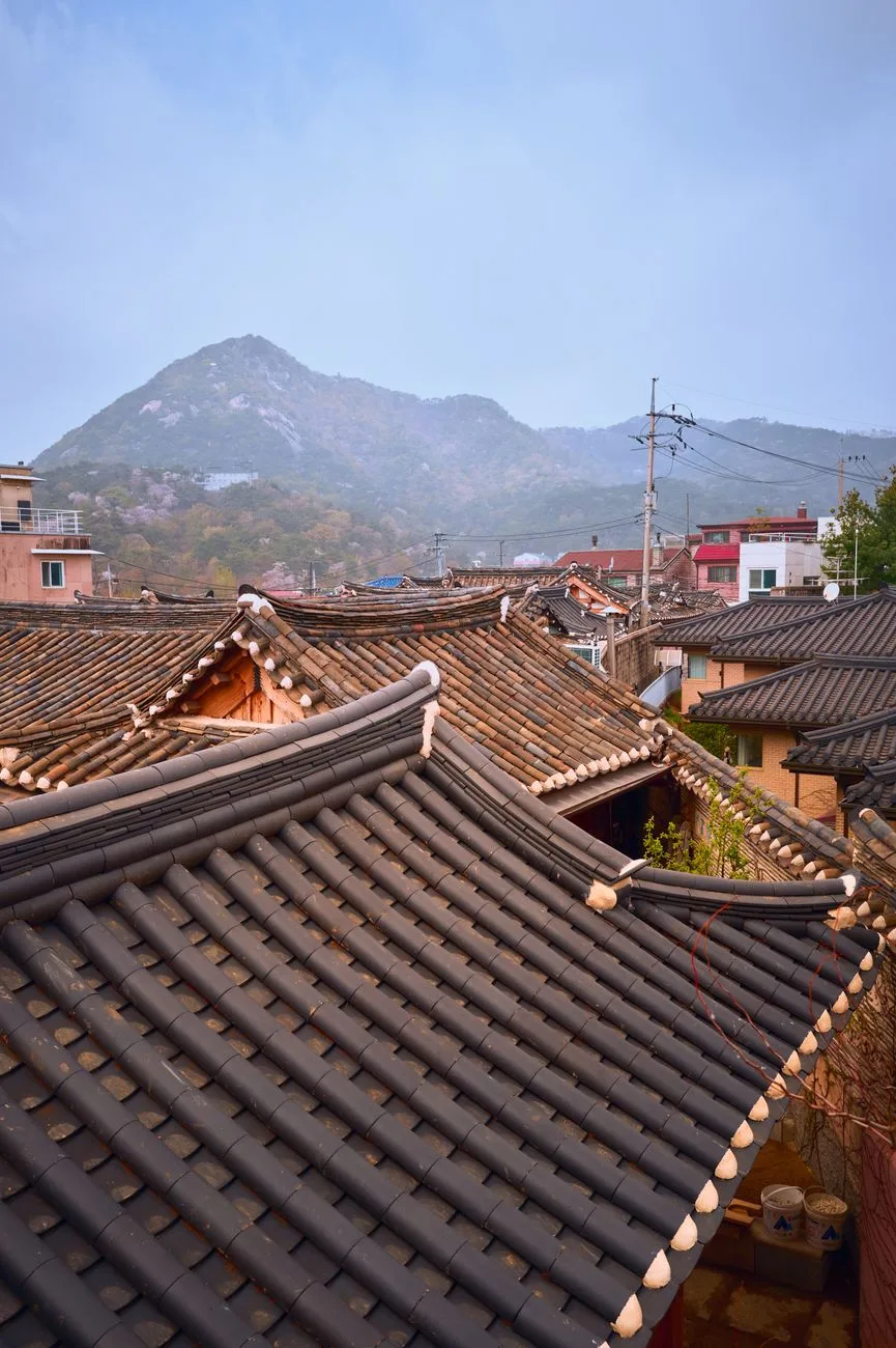 View of traditional Korean hanok rooftops with mountains in the background, showcasing cultural architecture.