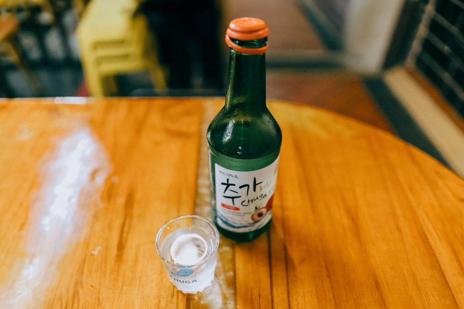 Korean soju bottle with shot glass on a wooden table in a cozy setting.