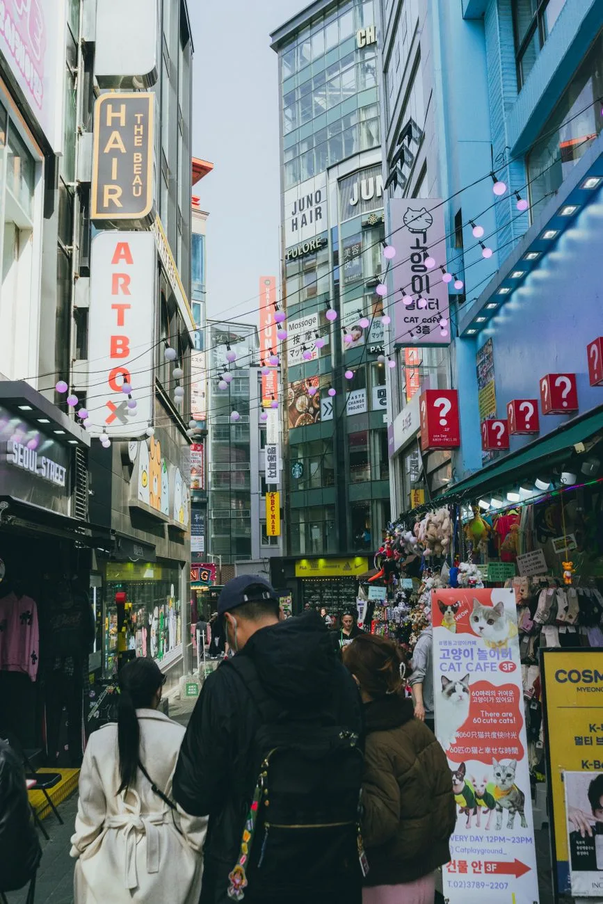 Bustling street view of Myeongdong in Seoul, showcasing shops and people amid vibrant signs and decorations.