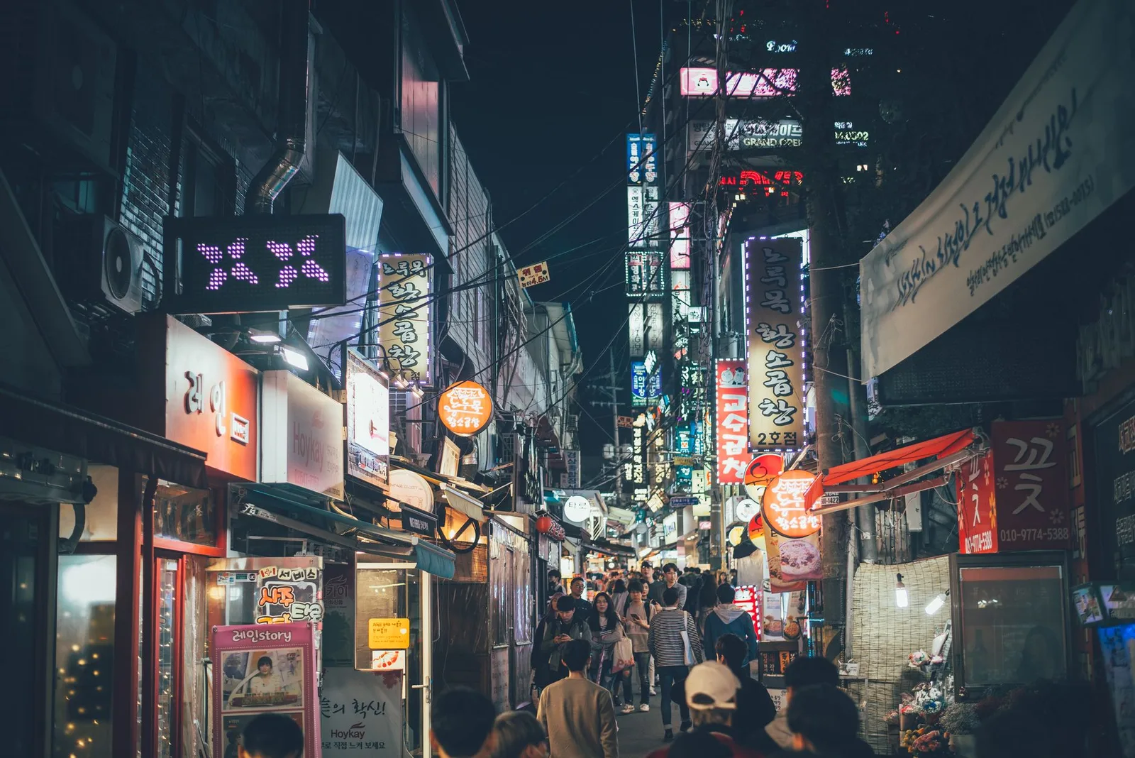Bustling night market street in Seogyo-dong, Seoul with neon lights and crowds.