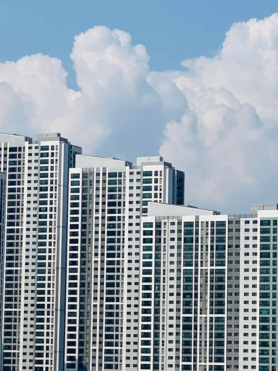 High-rise apartment buildings in Seoul under a clear blue sky with dramatic white clouds.