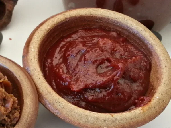 Gochujang is a finished product, not a spice: roughly a quarter red pepper powder, the rest glutinous rice, fermented soybean and salt. That is why it cannot be swapped gram-for-gram with gochugaru. Gochujang in a traditional earthenware pot — thick, glossy fermented chilli paste, not a loose powder