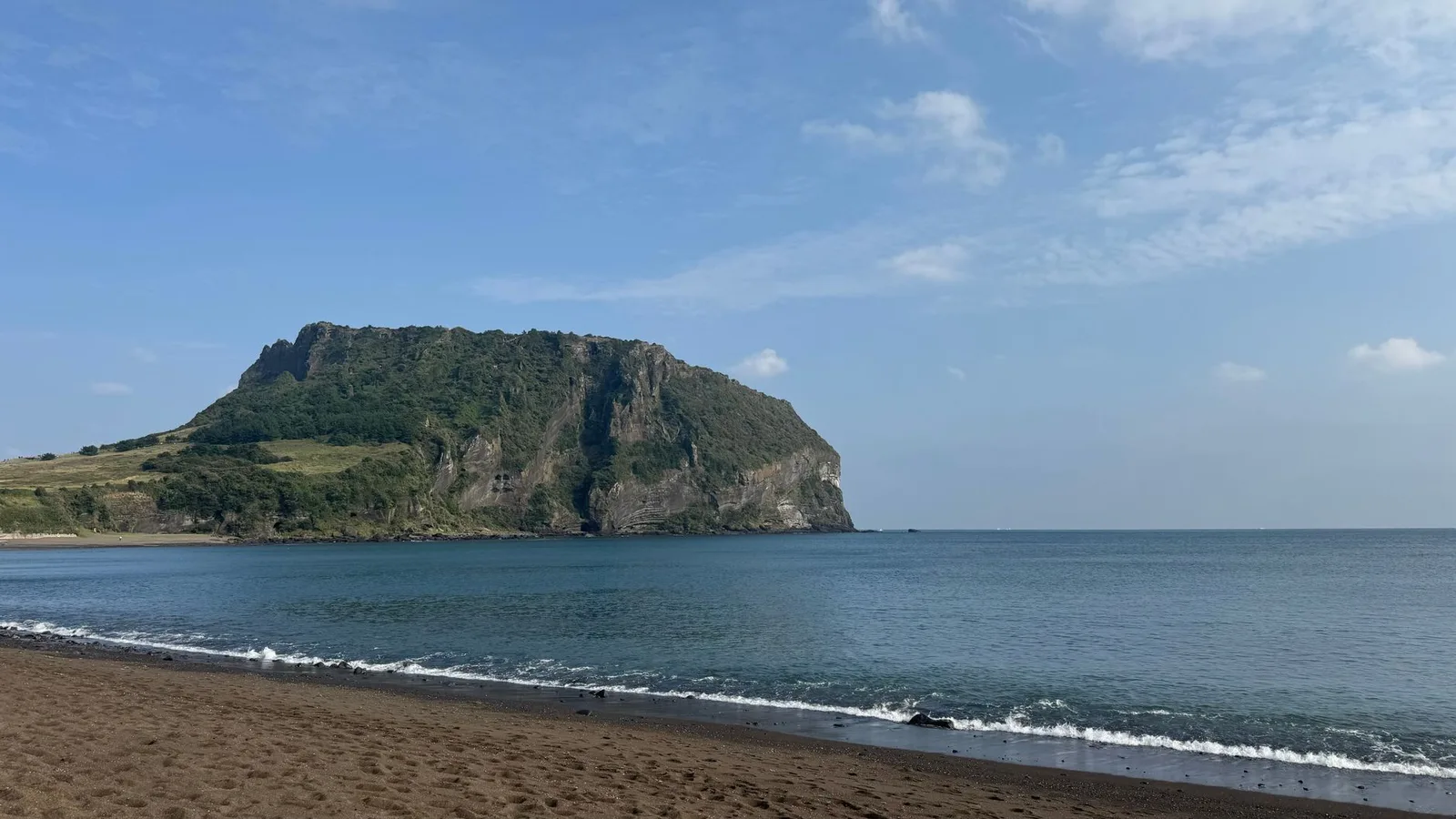 Peaceful beach view with Seongsan Ilchulbong peak on Jeju Island, South Korea.