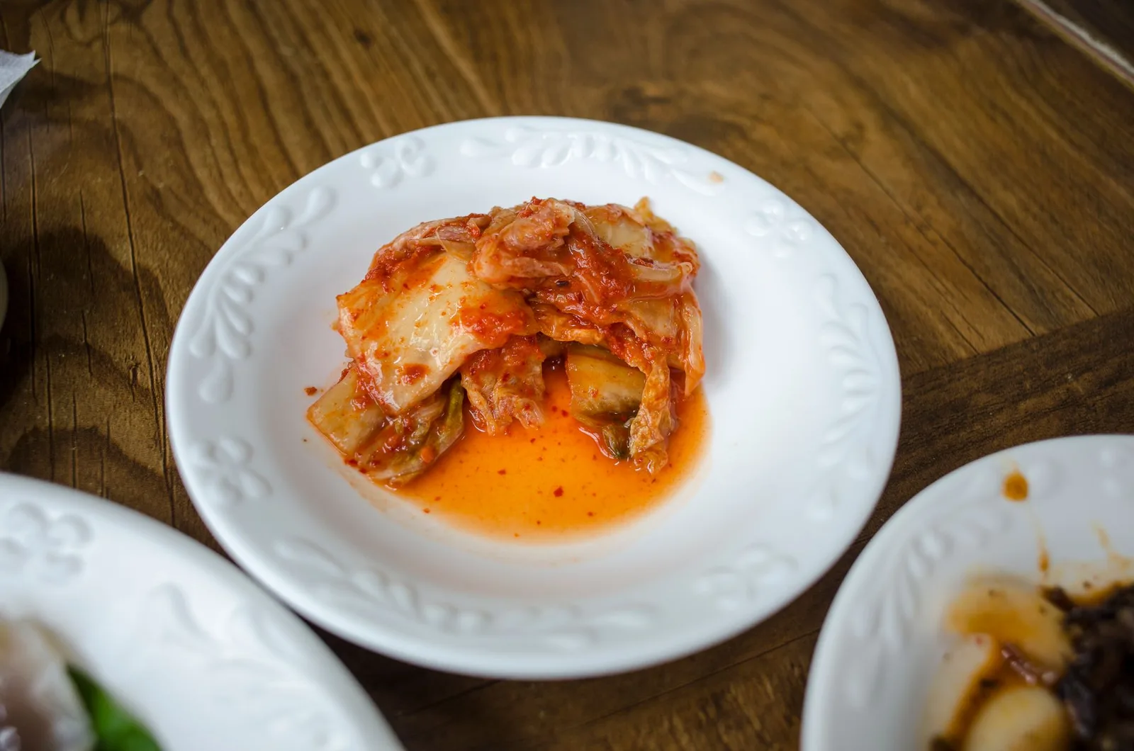 A close-up of traditional Korean kimchi served on a white ceramic plate on a wooden table.