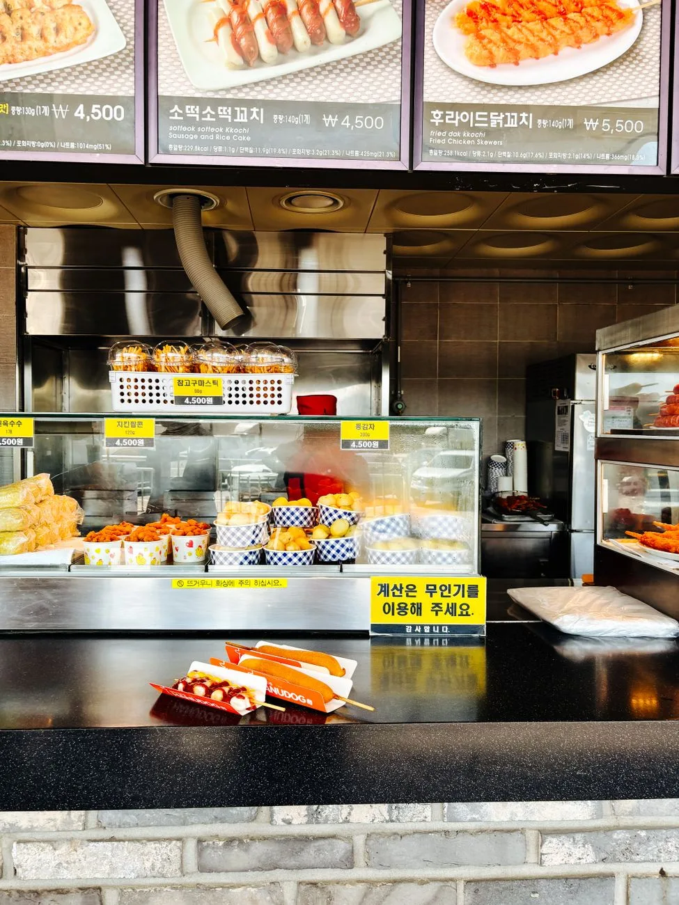 A vibrant Korean street food stall with assorted snacks like tteokbokki and hot dogs on display.