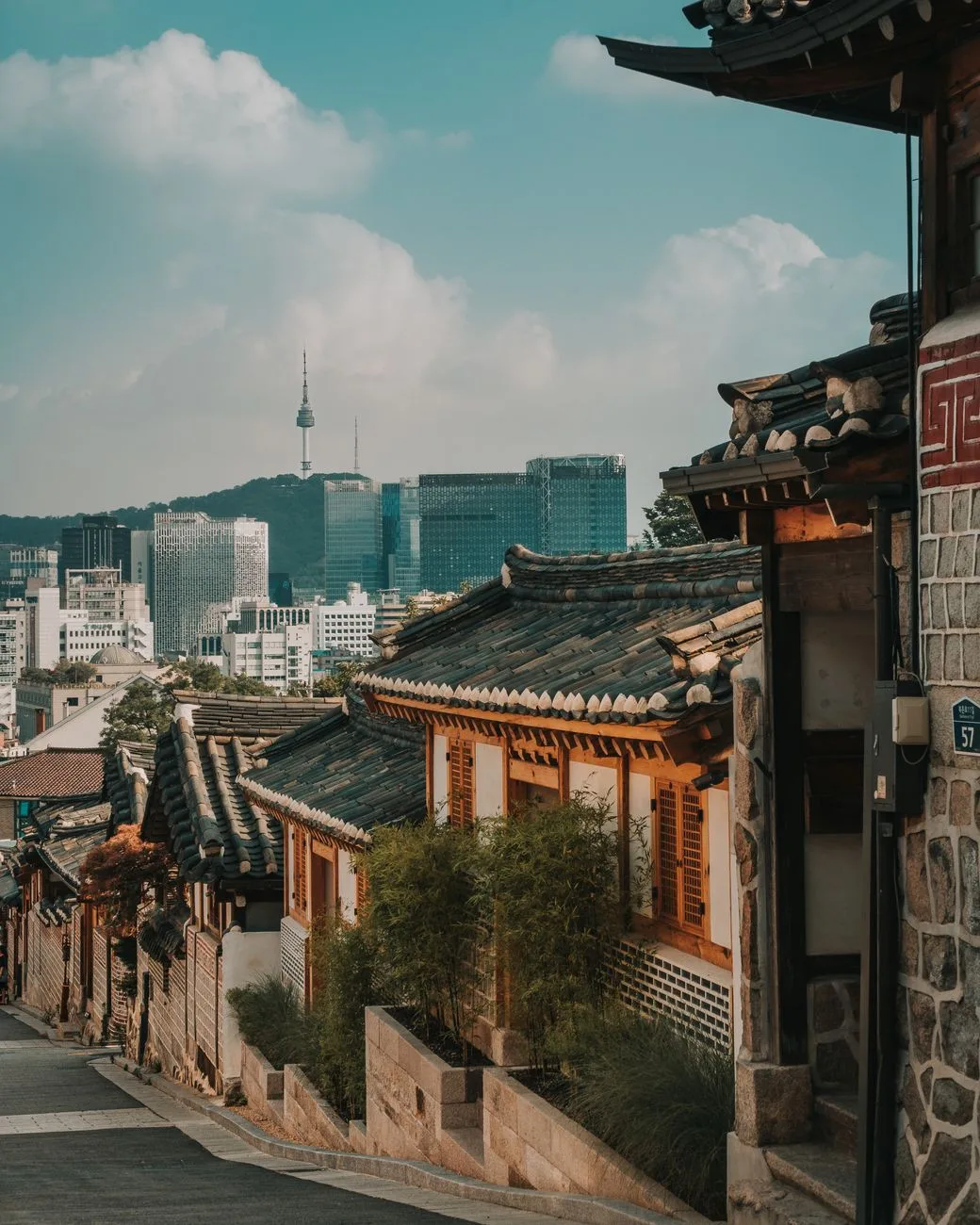 Charming view of Bukchon Hanok Village alley with modern Seoul skyline, blending traditional and contemporary architecture.