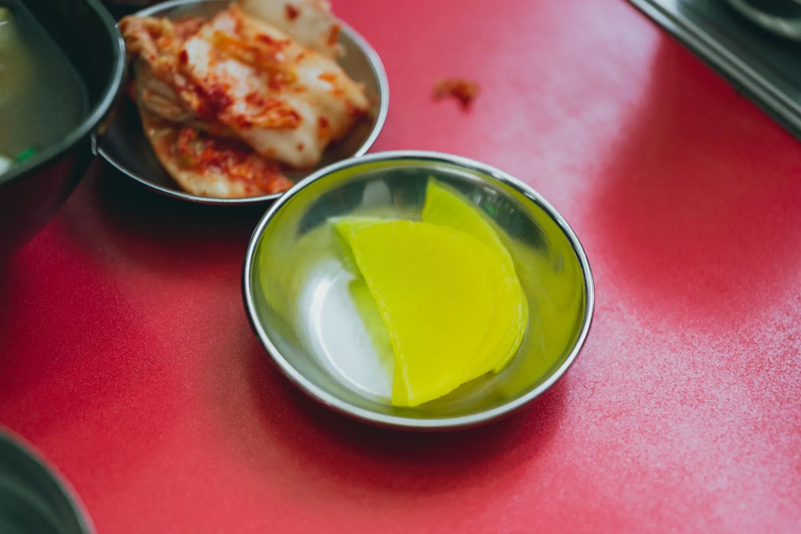 Vibrant Korean side dishes featuring kimchi and pickled radish on a red table in Seoul.