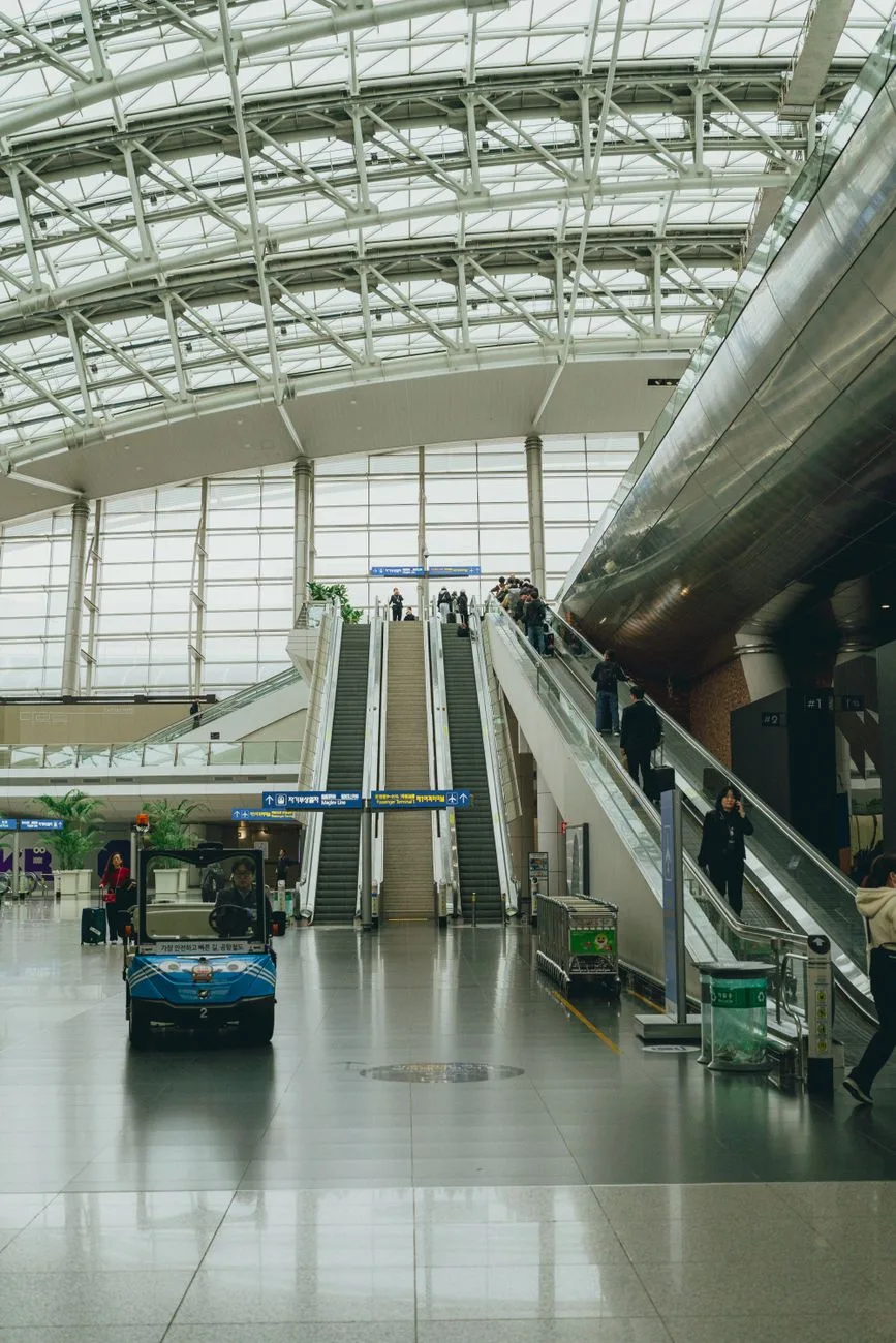 View of the interior of Seoul Incheon Airport with escalators and travelers.